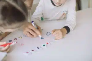 bambino che colora un foglio bianco con il pennarello, con l'aiuto di un adulto