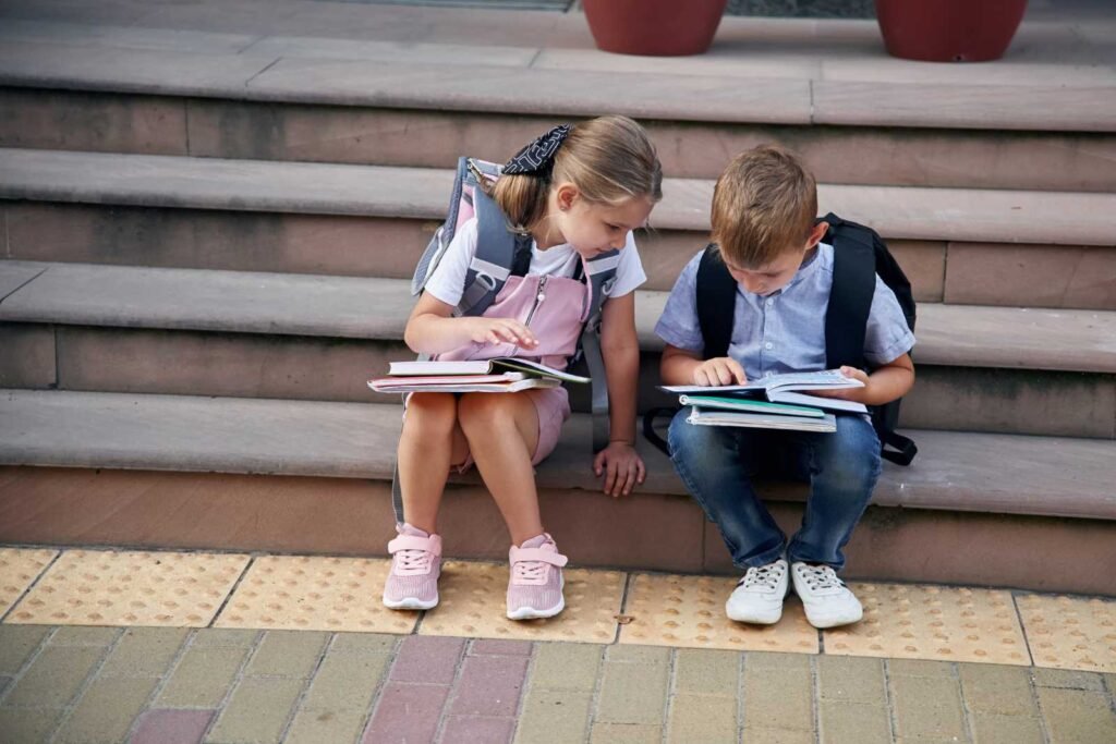 due alunni, maschio e femmina, sulle scale della scuola leggono sui quaderni