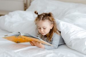 Bambina che legge un libro a letto, immagine collegata ai segnali precoci della dislessia e alle difficoltà di lettura nei bambini