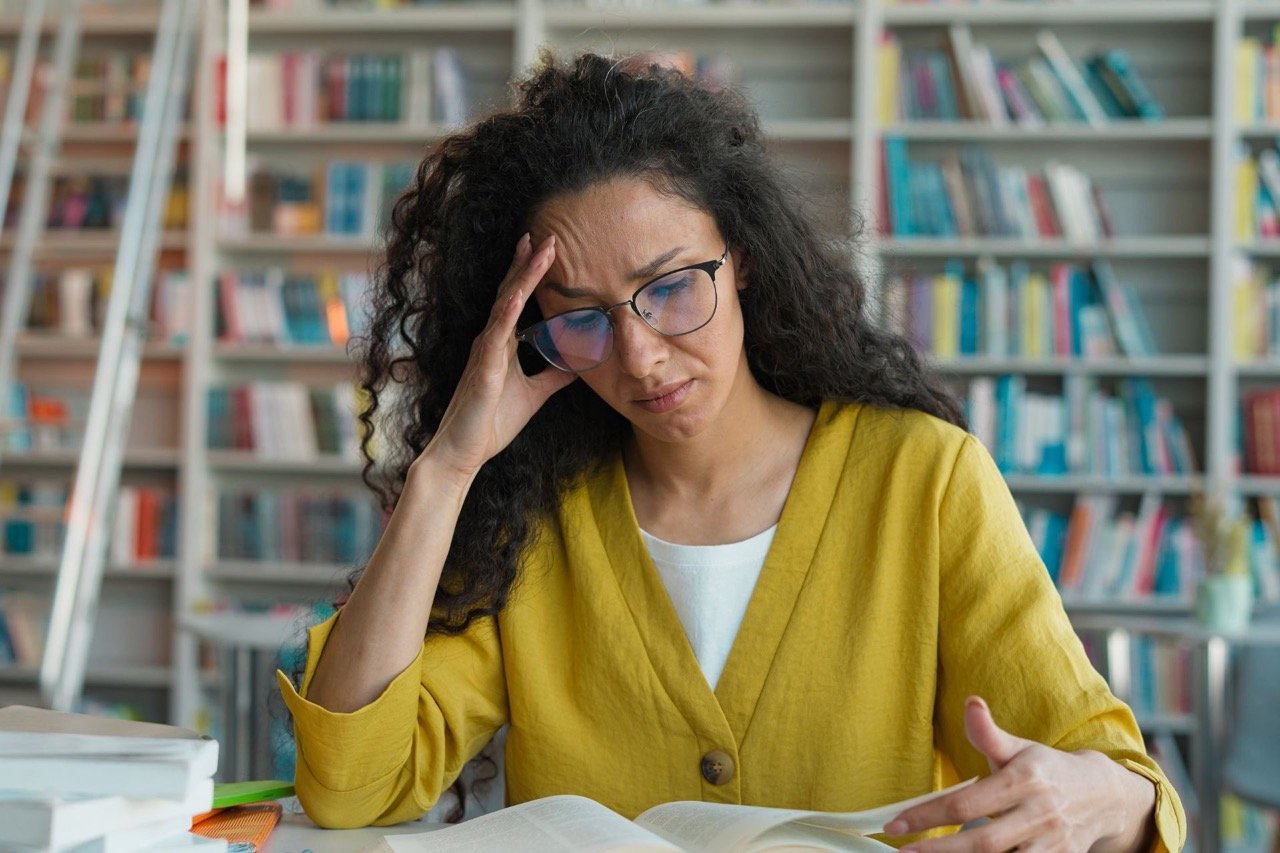 Donna adulta affaticata durante la lettura di un libro in biblioteca